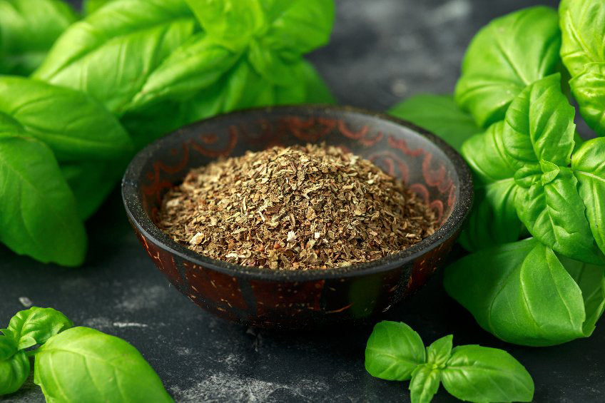 Wooden bowl of dried basil surrounded by fresh basil leaves