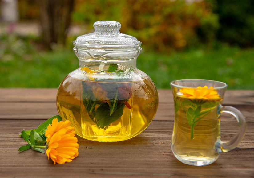 Transparent teapot and a cup of calendula tea on a wooden table