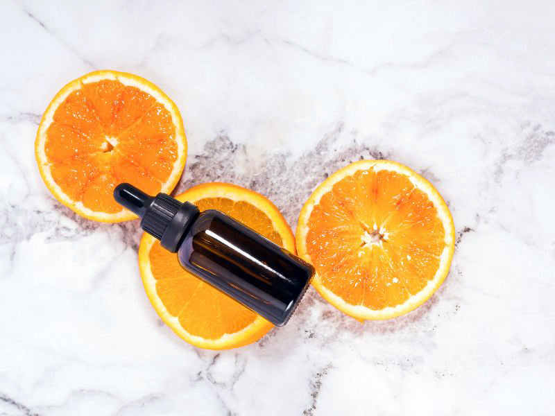 amber glass facial serum bottle with fresh orange slices