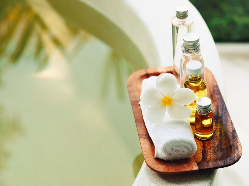 bath oils on wooden tray with washcloth next to tub