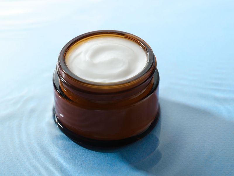 anhydrous cream in amber glass jar surrounded by blue water